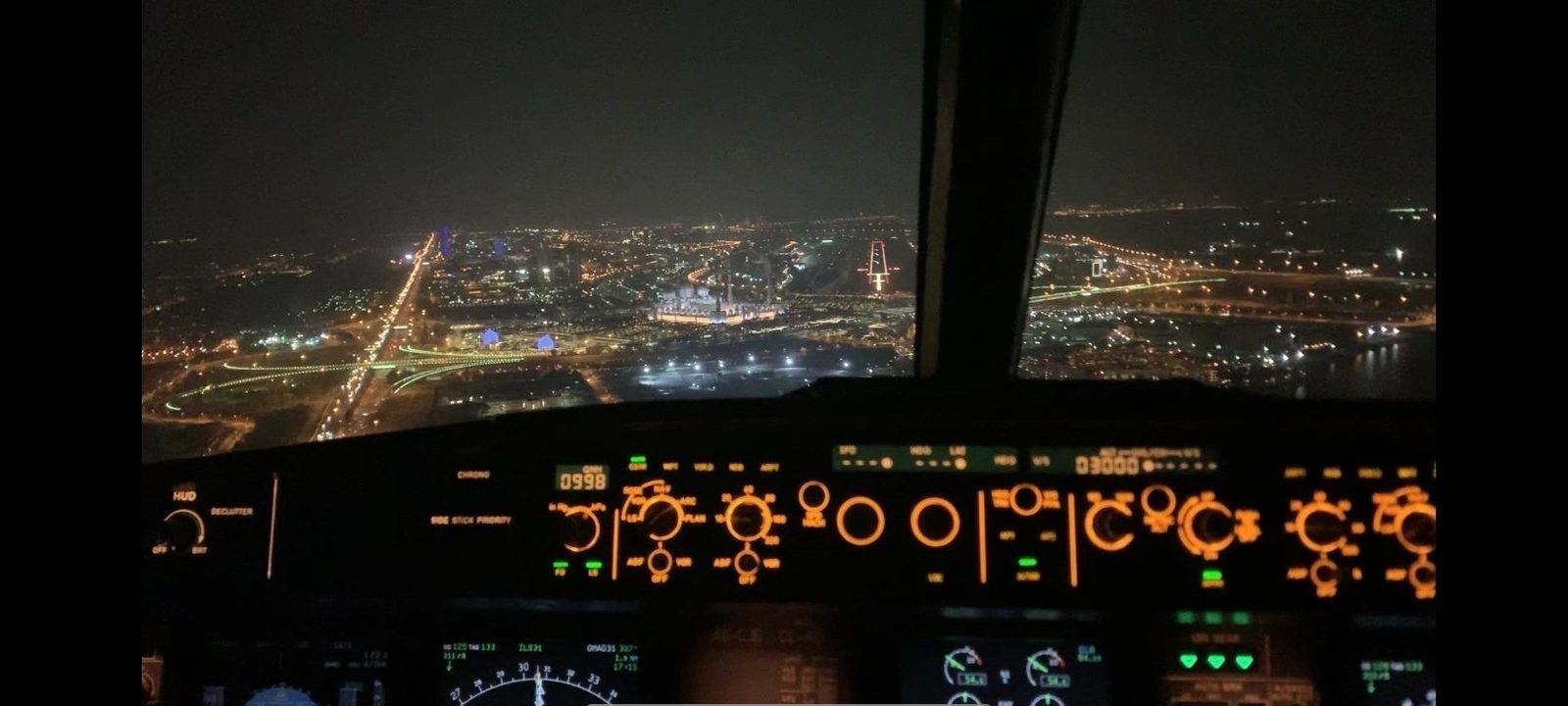 View from an airliner flight deck at night with city lights below