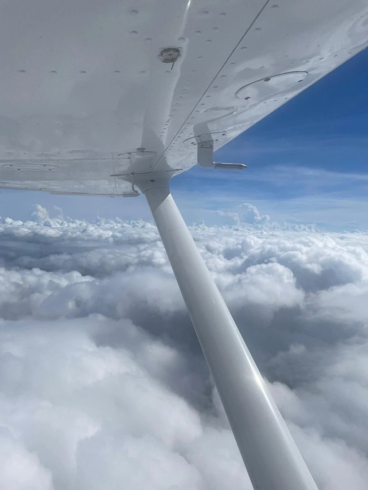 The wing and strut of a high-wing aircraft above a layer of cloud